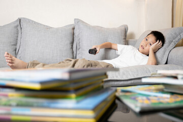 Student lying on sofa,watching cartoons on TV while studying,child boy is not interested in reading,No concentration on study,ADHD symptom or relaxing after learning,lifestyle,relaxation and education