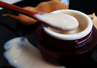 Scoop skin cream in a red jar, tamarind fruit, and pour the cream over the black background.

