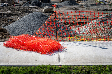 Fresh new orange safety fencing being set up next to sidewalk around a construction site of dirt...