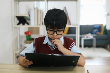 Schoolboy think hard while sitting at desk doing homework.