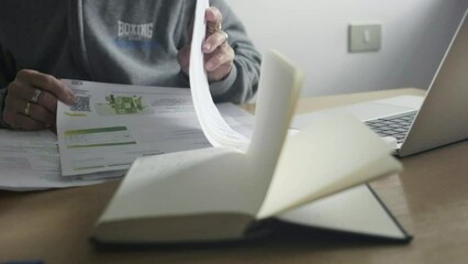 Closeup shot, female elder hands go through paper payment bills, desktop office with laptop