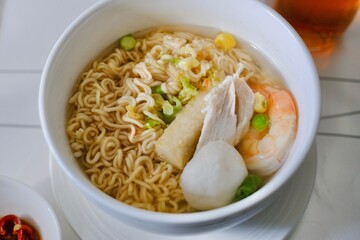 A bowl of egg ramen noodles with chicken breast, prawn, bean curd, fish ball and Asian vegetables on a business class flight from Sydney to Kuala Lumpur, with chilli soy sauce and glass of oolong tea
