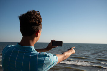 A young attractive guy is posing while relaxing on the sea and taking a photo with his phone.