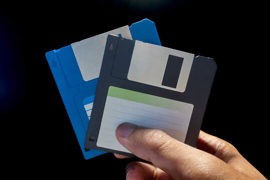 Close up view of hand holding two floppy disks on a dark background