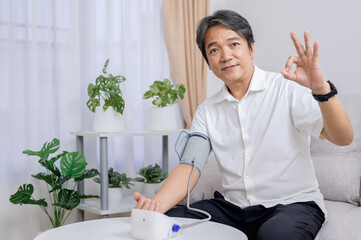 A healthy Asian elderly man uses a blood pressure monitor at home to self-test his blood pressure...