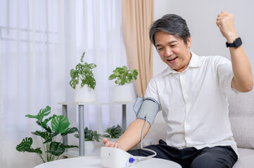 A healthy Asian elderly man uses a blood pressure monitor at home to self-test his blood pressure...