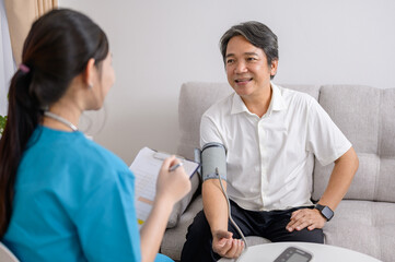 A young Asian female nurse talks and asks about the condition of an elderly male patient. Use a blood pressure monitor to test the pressure level to test for diabetes and high blood pressure.