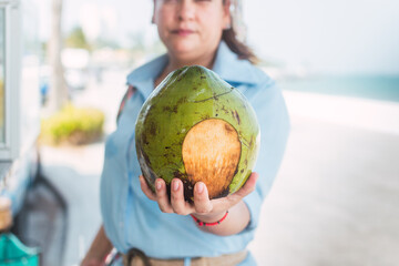 Fototapeta premium Latin woman drinking coconut water on the beach, at a street stall with glasses of tropical fruits.