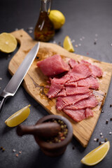 Woman cut tuna steak into slices on a wooden cutting board at domestic kitchen cooking tuna carpaccio