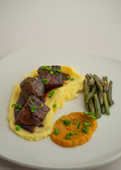 baked horse meat with demi-glace sauce, mashed potatoes and young beans on a gray background