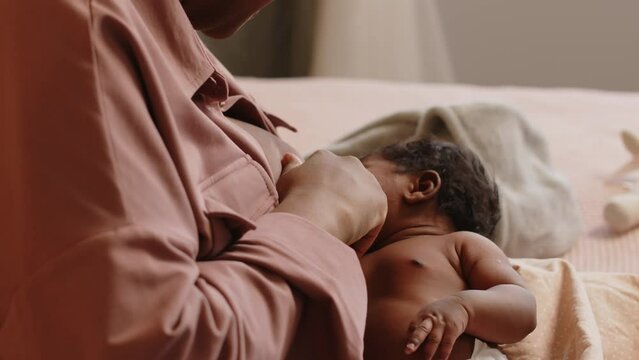 Cropped shot of loving mother breastfeeding tiny baby on bed in their cozy apartment