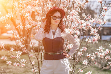 Magnolia park woman. Stylish woman in a hat stands near the magnolia bush in the park. Dressed in...