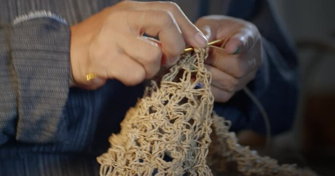 Slow motion scene while an Asian female artisan who is a local villager knitting folk basket made from leftover paper band to sell as extra income in the basketry shop shop.
