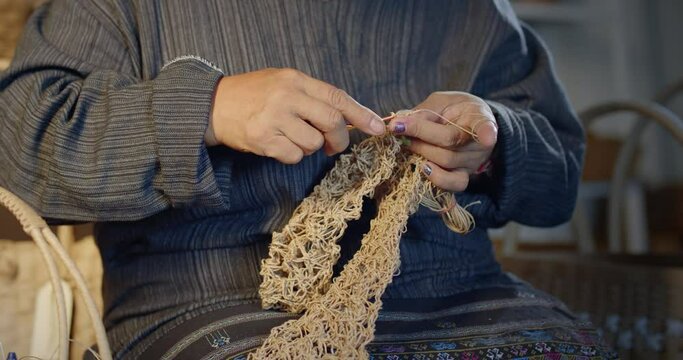 Slow motion scene while an Asian female artisan who is a local villager knitting folk basket made from leftover paper band to sell as extra income in the basketry shop shop.