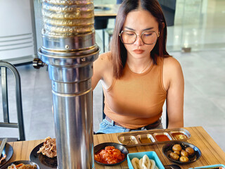 Focused young woman dining alone at a samgyupsal restaurant, surrounded by an assortment of traditional Korean side dishes.