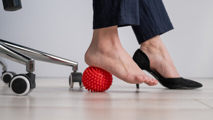 Business woman massages her feet on a massage ball with spikes.
