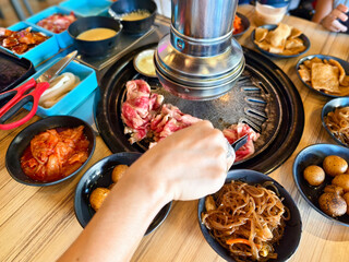 Dining experience captured at a Korean samgyupsal restaurant with fresh meats, kimchi, side dishes, and a portable grill.