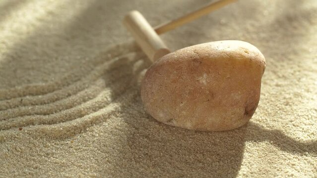 Close-up making zen garden with sand and stone using mini bamboo wooden rake