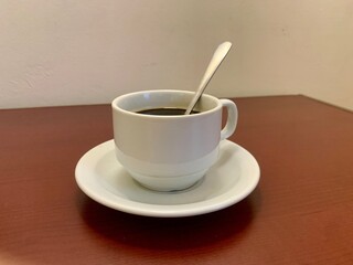 White cup of black coffee on the brown table