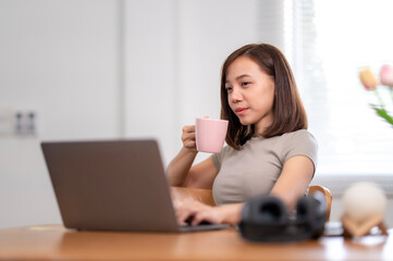 A woman is sitting at a desk with a laptop and a pink mug of coffee