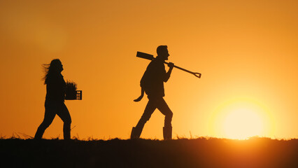 Obraz premium A couple of farmers with equipment walks through a field at sunset.