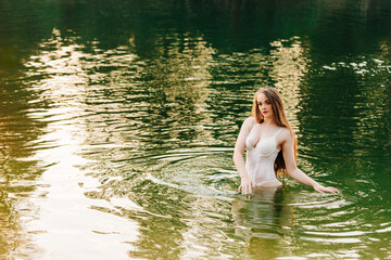 Gorgeous millennial female in white lingerie standing in river