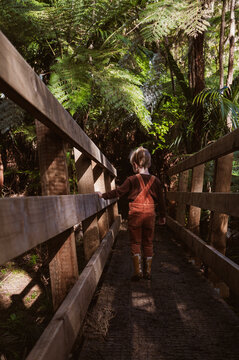 Child walking across bridge in forest with muddy yellow boots