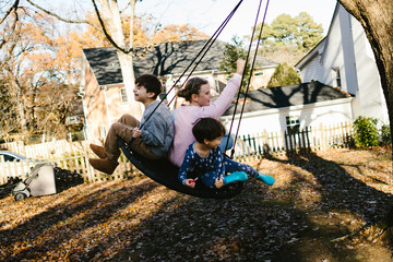 Kids laughing together on tree swing in front of home in fall