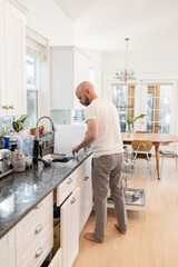 Man rinsing dishes in brightly lit kitchen