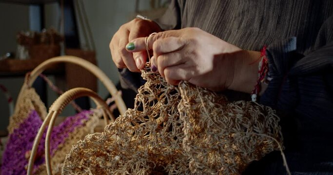 Slow motion scene while an Asian female artisan who is a local villager knitting folk basket made from leftover paper band to sell as extra income in the basketry shop shop.