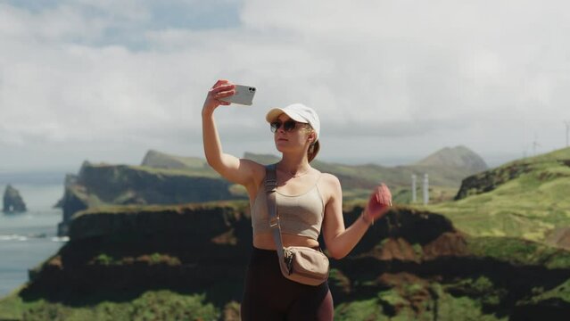 Travel Girl in Sunglasses Taking Selfie in front of Ocean Coast and Green Cliffs during Windy Day