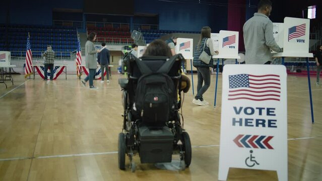 Woman with physical disability in electric wheelchair comes to vote in polling station. American citizens during political races of US presidential candidates. National Election Day in United States.