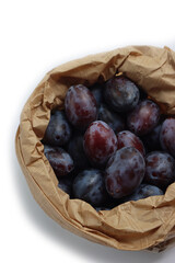 Close-up of purple plums in a brown paper bag isolated on white background. Prunus domestica  fruits