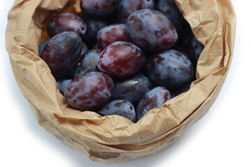 Close-up of purple plums in a brown paper bag isolated on white background. Prunus domestica  fruits