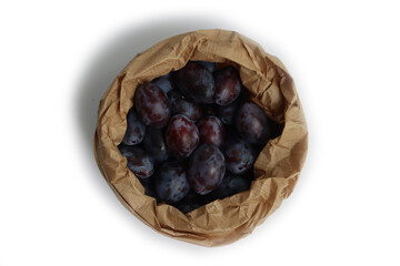Close-up of purple plums in a brown paper bag isolated on white background. Prunus domestica  fruits