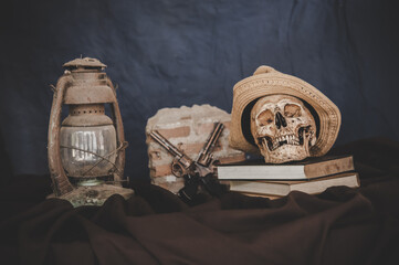 Still life with the skulls in books, old lamps and guns crossed.