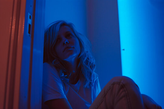 A melancholic scene of a woman sitting in solitude under a blue light, portraying a sense of sadness