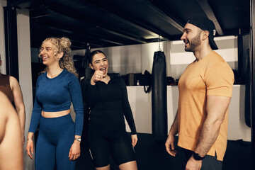 Laughing young woman in sportswear giving a thumbs up while standing with a diverse group of people after an exercise class together in a gym