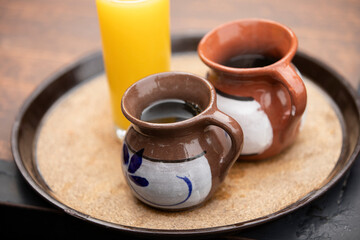 Two cups of special Mexican coffee, café de olla, served in clay cups alongside a glass of orange juice on a  tray in Bernal, Querétaro, Mexico.