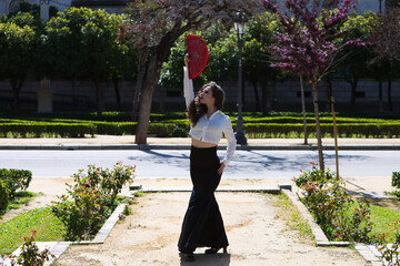 Beautiful woman with long curly hair, dancing flamenco with a red fan, she is in Seville, Spain....