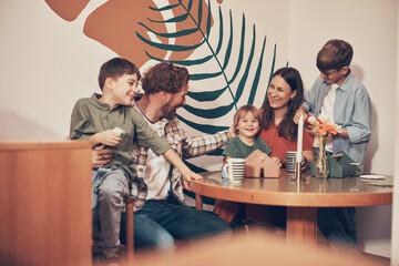 Laughing mother and father sitting with their three cute young sons in an arts and crafts cafe during a family bonding activity together
