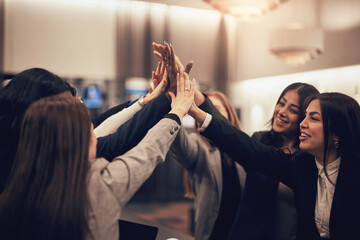 Laughing businesswomen high-fiving in a hotel lobby during a meeting together
