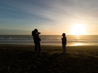 Female capturing a man on the beach during sunset