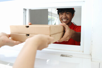 Young worker in red uniform serving two boxes of pizza for customer to take away.