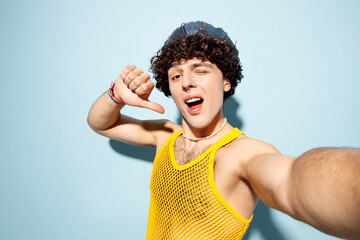 Close up young cool gay Latin man wear mesh tank top hat clothes do selfie mobile cell phone shot point on himself wink isolated on plain blue background studio Pride day June month love LGBT concept