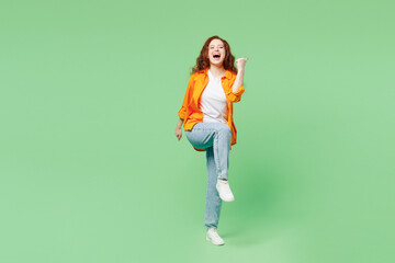 Full body young ginger woman wear orange shirt white t-shirt casual clothes doing winner gesture celebrate clenching fists say yes isolated on plain pastel light green background. Lifestyle concept.