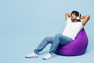 Full body young happy Indian man wear white t-shirt casual clothes sit in bag chair listen to music...