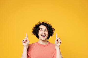 Young smiling happy fun man he wear pink t-shirt casual clothes point index finger overhead on empty blank area workspace isolated on plain yellow orange background studio portrait. Lifestyle concept.