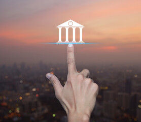 Hand pressing bank flat icon over blur of cityscape on warm light sundown, Business banking online...
