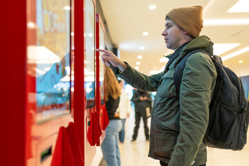 Man interacts with digital kiosk in modern mall, navigating touch screen. Technological integration...